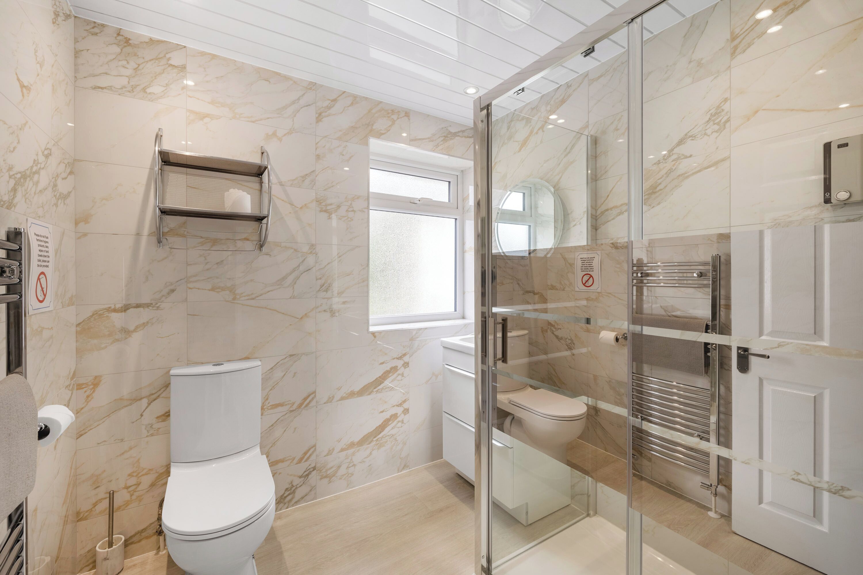 Une salle de bain moderne avec des toilettes, une douche à parois de verre et un mur en marbre.