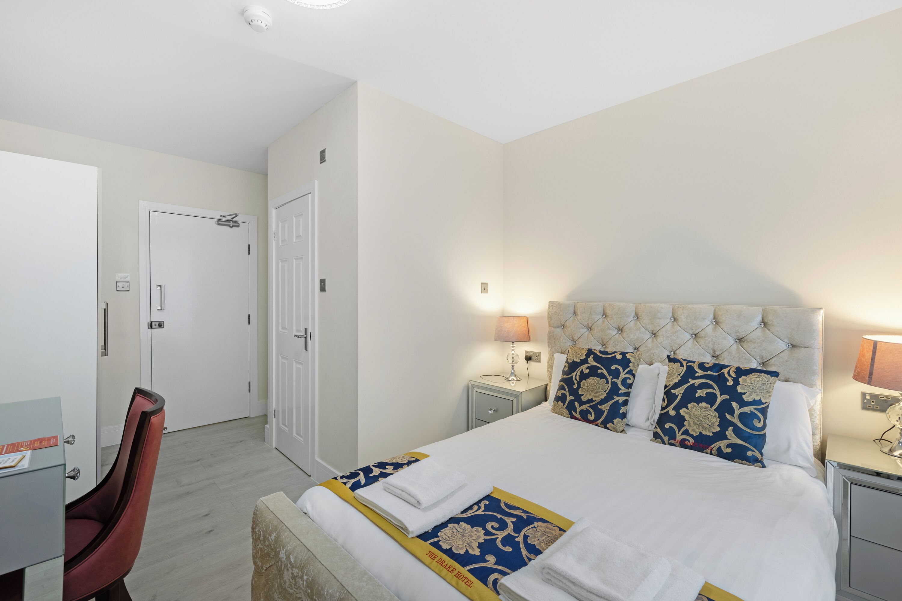 A hotel room with a bed, bedside tables, a chair, and a desk.
