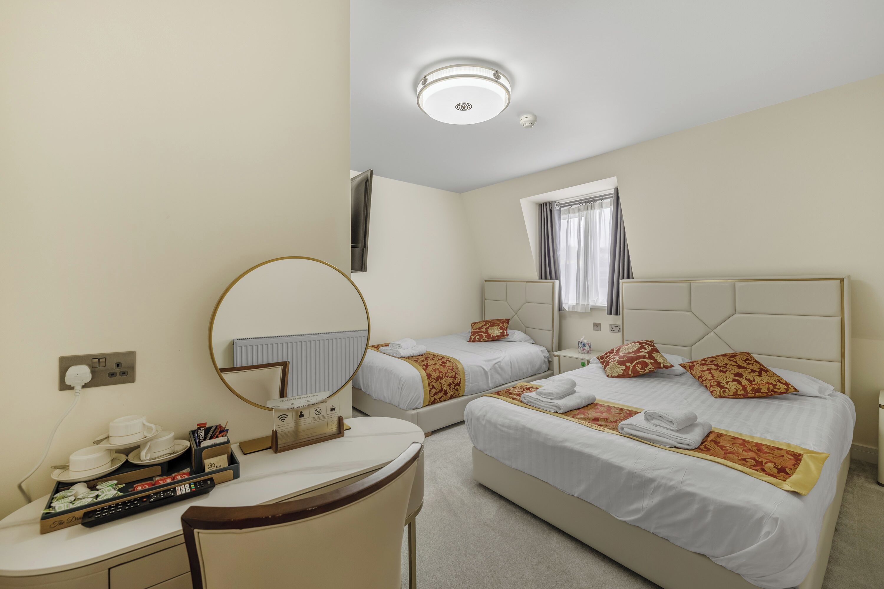 A hotel room with two beds, a desk with a telephone, a mirror, and a window with curtains.