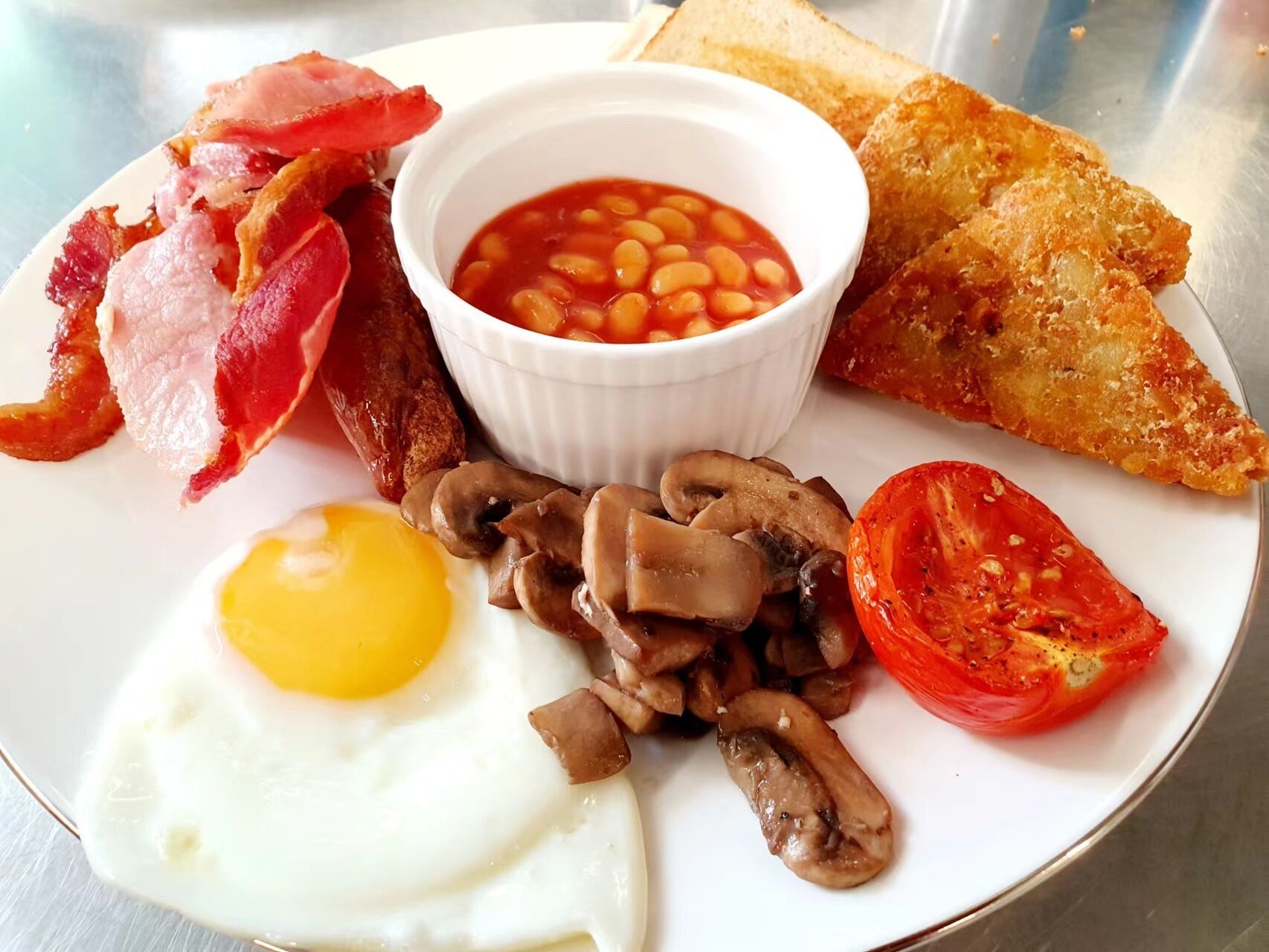 A plate with bacon, beans, fried egg, mushrooms, tomato, and toast.