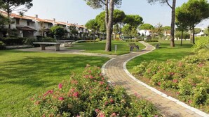 A well-maintained park with a paved walkway, benches, and flowering bushes. - Villa in village with swimming pool 6 beds (Bibione)