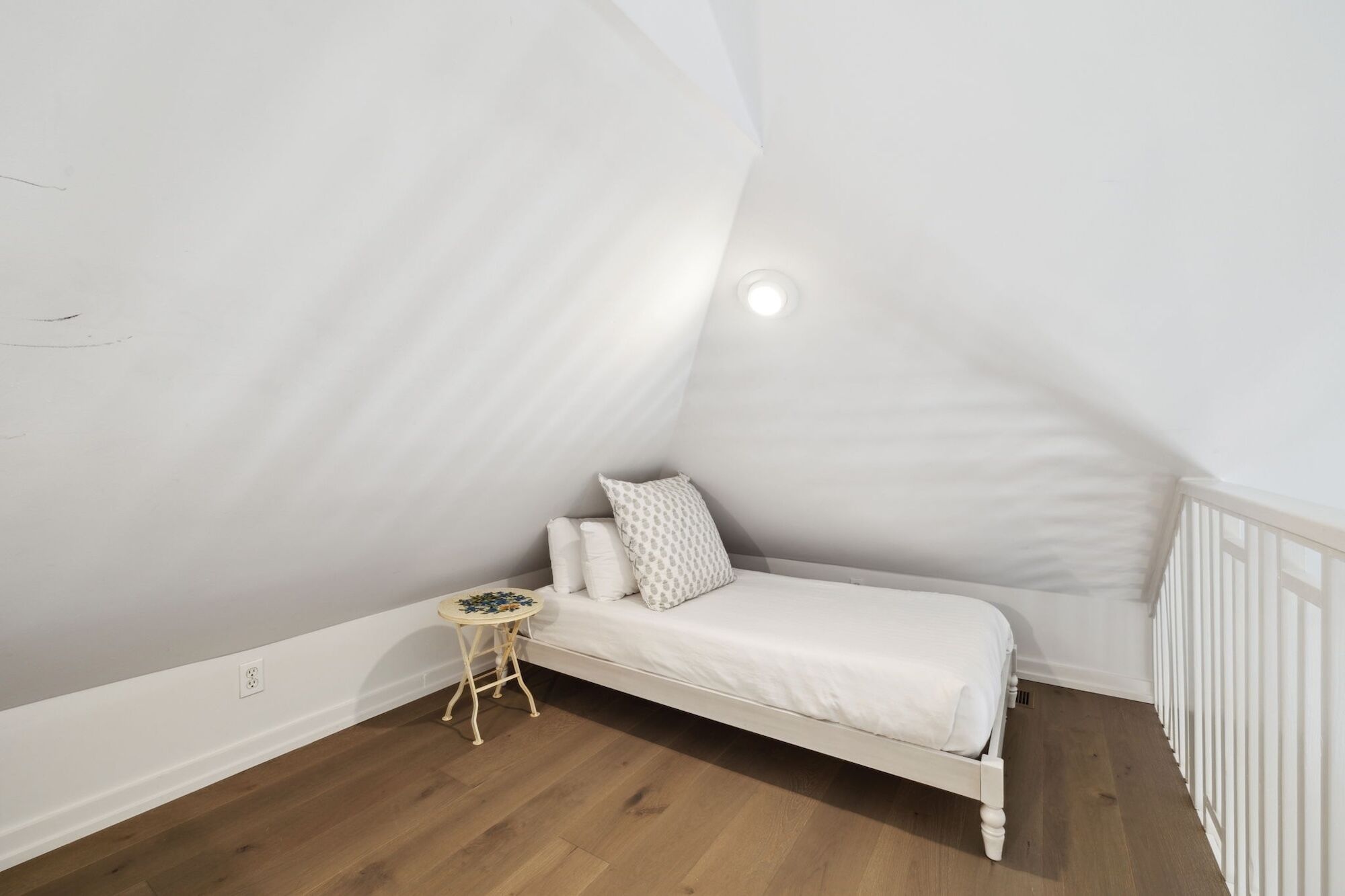 A small, white, sloped-roof bedroom with a single bed, a small round table, and a radiator.