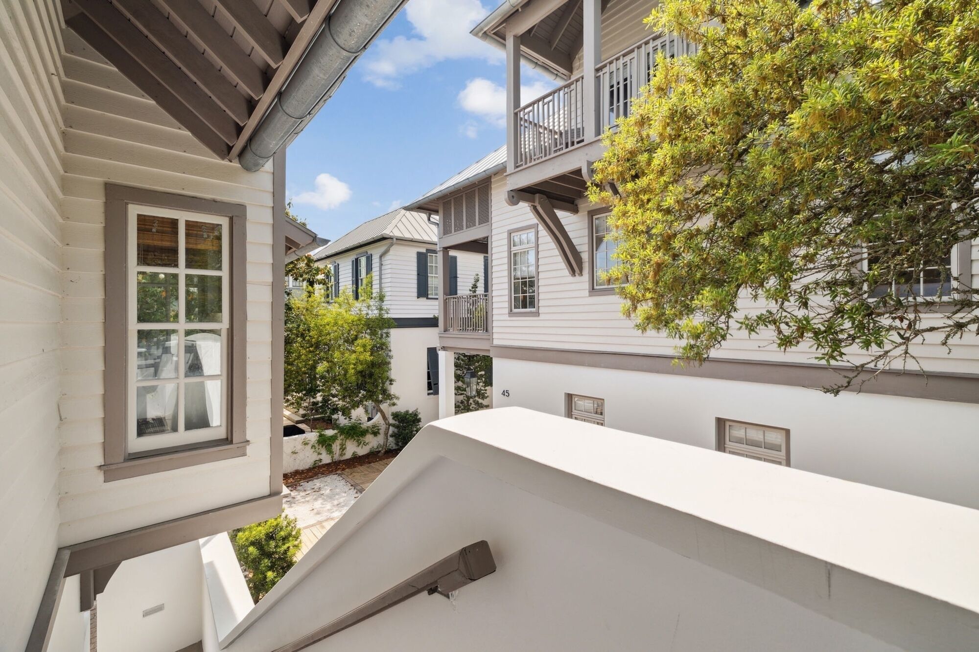 A multi-story residential building with a white exterior, multiple balconies, and a tree in the courtyard.