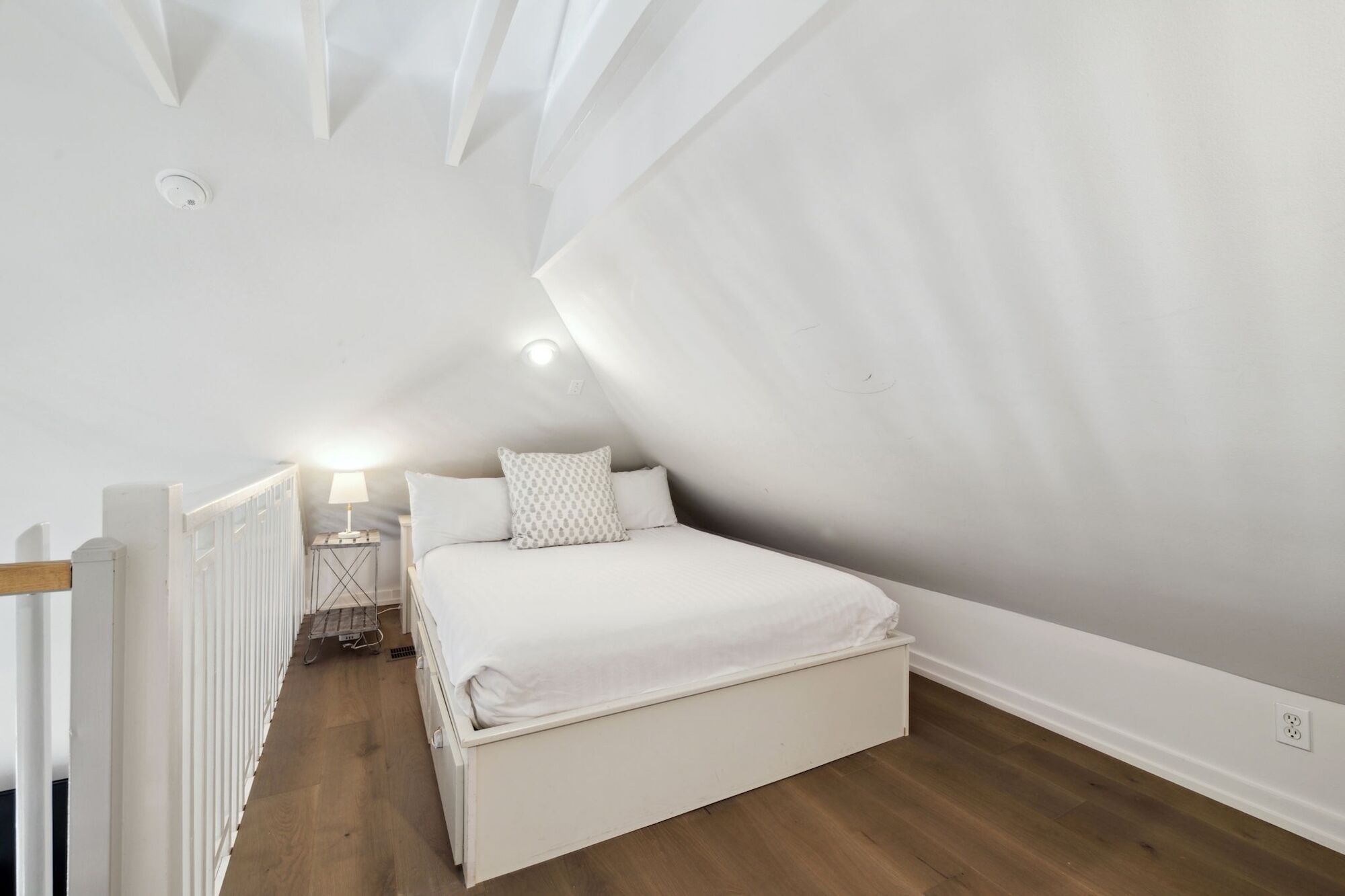 Une chambre avec un plafond en pente, un lit simple, une table de chevet avec une lampe et un radiateur.