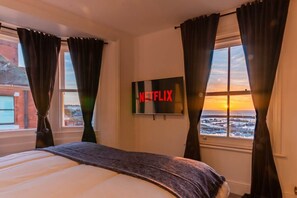 A hotel room with a bed, a TV mounted on the wall, and a view of a cityscape through a window. - Luxury Ramsgate Harbour View Maisonette By Adliv (Ramsgate)