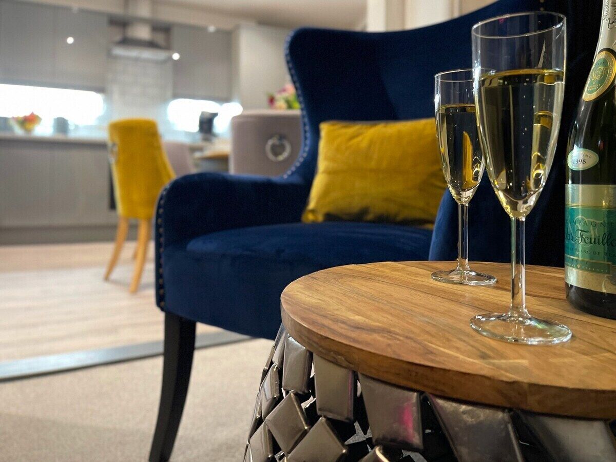 Een moderne woonkamer met een blauwe bank, gele kussens en twee glazen witte wijn op een houten tafel.