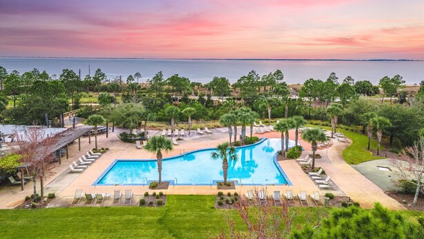 Ein Resort mit großem Pool, Liegestühlen und Blick auf den Ozean bei Sonnenuntergang.