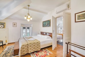 A bedroom with a bed, a wooden floor, a chandelier, a door, and a window. - Piccolo Mondo Antico: Stresa 2BR Apartment With Lake View (Stresa)