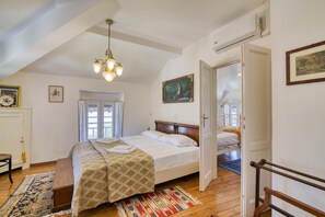 A bedroom with a bed, a wooden floor, a chandelier, a door, and a window.