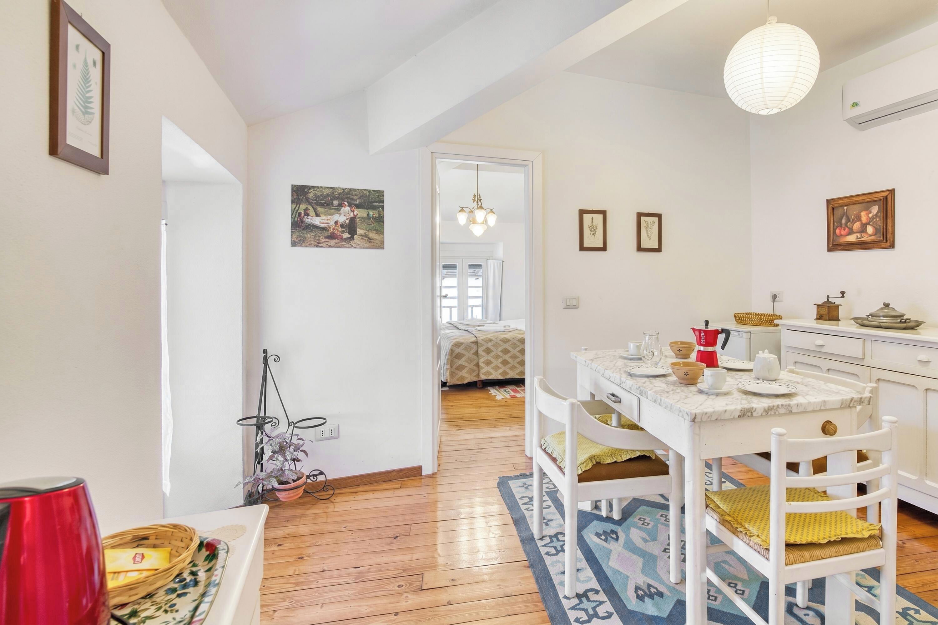 Un cuarto acogedor con piso de madera, una mesa de comedor con sillas, una zona de cocina y una cama al fondo.