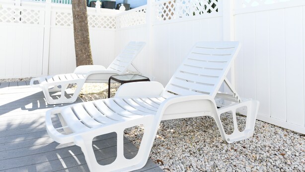 Two white lounge chairs with a small table, set on a wooden deck with pebbles, against a white fence. - 4 BR Beach House with a Private Pool & Steps to the Beach! Seaborn (Surfside Beach)