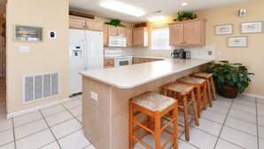 A kitchen with a central island, wooden cabinets, a refrigerator, microwave, and a stove. There are four bar stools and a large potted plant. - 4 BR Beach House with a Private Pool & Steps to the Beach! Seaborn (Surfside Beach)