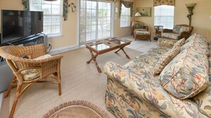A living room with a television, wicker furniture, a sofa with floral upholstery, and a ceiling fan. - 4 BR Beach House with a Private Pool & Steps to the Beach! Seaborn (Surfside Beach)