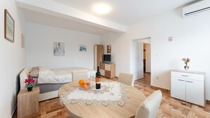 Een moderne, goed verlichte kamer met een ronde eettafel, een bank, een televisie en een kitchenette.
