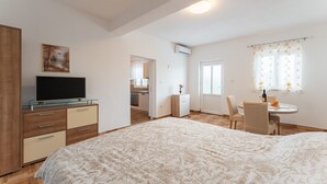 Een slaapkamer met een bed, een televisie, een bureau en een stoel. Er is een raam met gordijnen en een deur naar een badkamer.