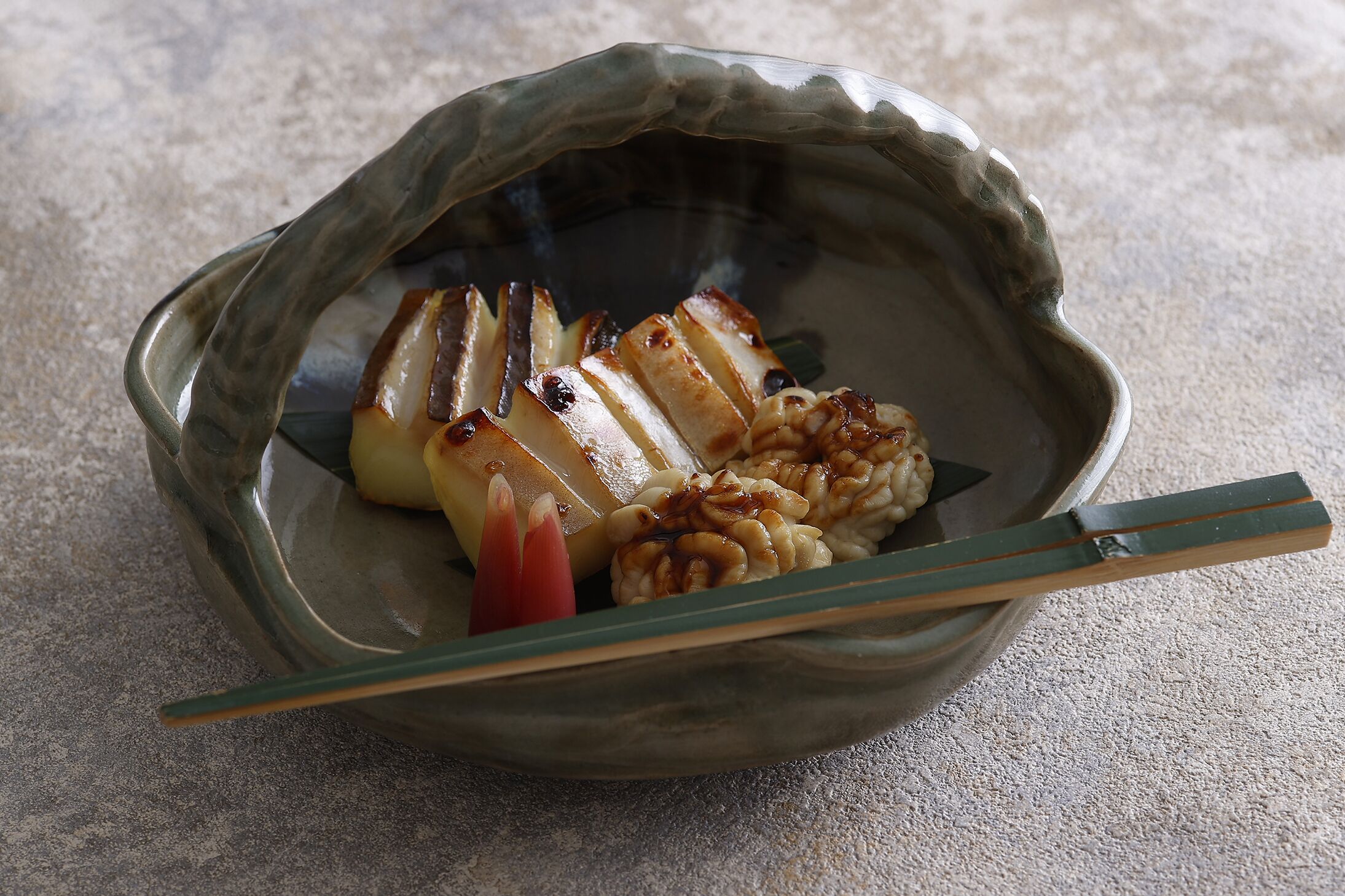 A ceramic dish with grilled food items and chopsticks.
