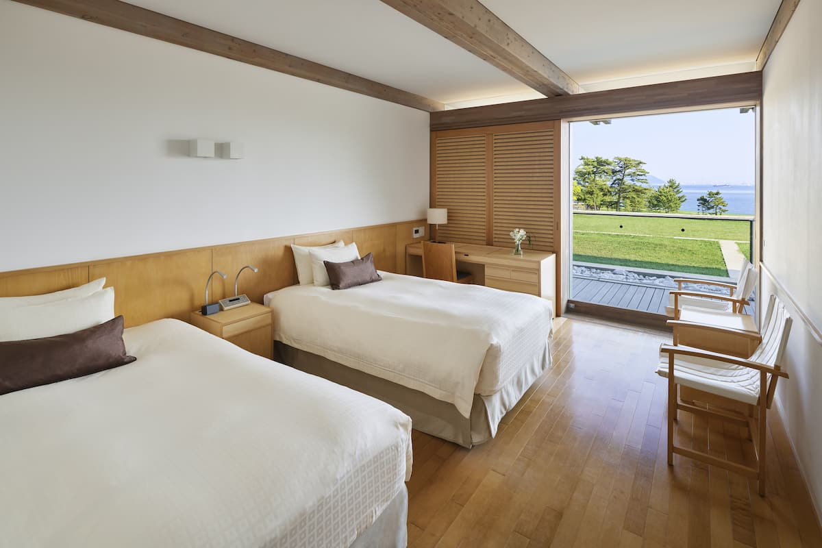 Une chambre d’hôtel avec deux lits, un bureau, une chaise et une vue sur l’extérieur.