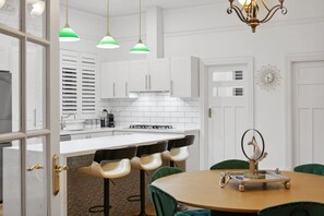 A modern kitchen with white cabinets, a central island, bar stools, and pendant lighting. - The Sapphire · 3BR Art Deco · Arcade · Fenced Yard (Inglewood)