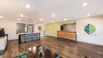 A spacious room with a wooden floor, a reception desk, and a dining area with chairs and a table.