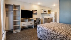 Ein Schlafzimmer mit Bett, Schreibtisch, Stuhl, Fernseher, Mikrowelle und Kühlschrank.