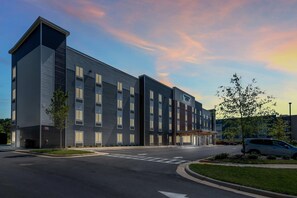 En modern hotellbyggnad med ett platt tak, många fönster och en parkeringsplats framför.