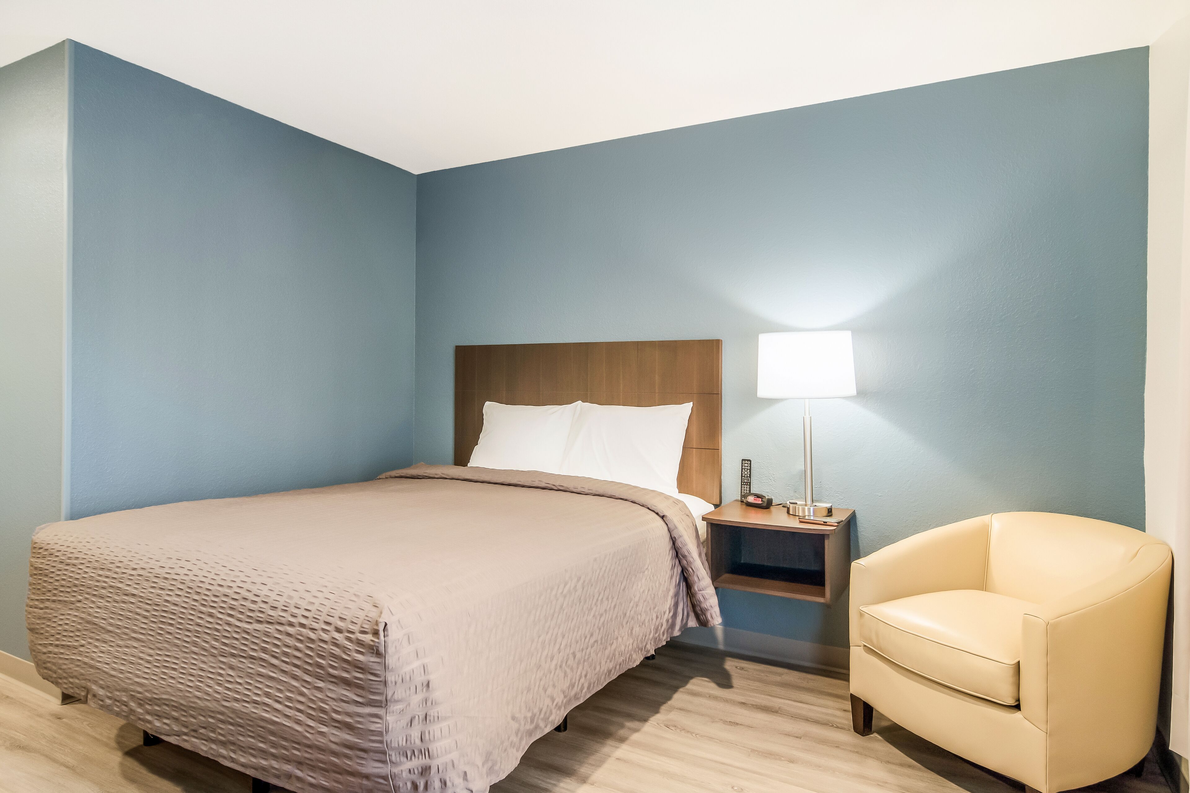 Una camera d'albergo con un letto, un comodino, una lampada e una sedia.