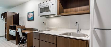 A compact kitchen with wooden cabinets, a microwave, a sink, and a refrigerator.