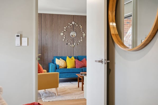 Un salon moderne avec un canapé bleu, des coussins colorés, un plancher en bois et un élément décoratif mural.