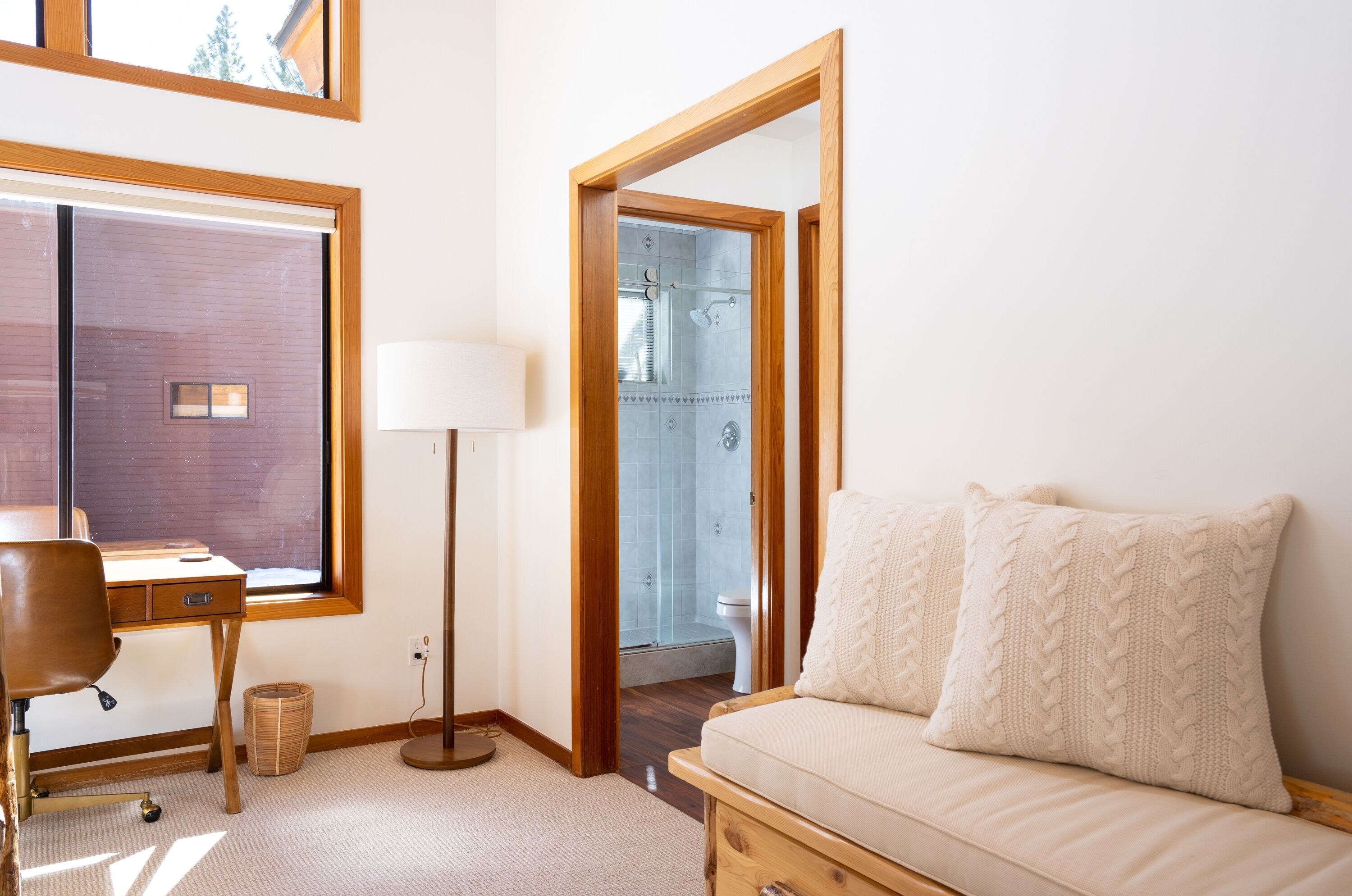 A bedroom with a wooden desk, a chair, a bedside table, a lamp, a sofa, and a large mirror.