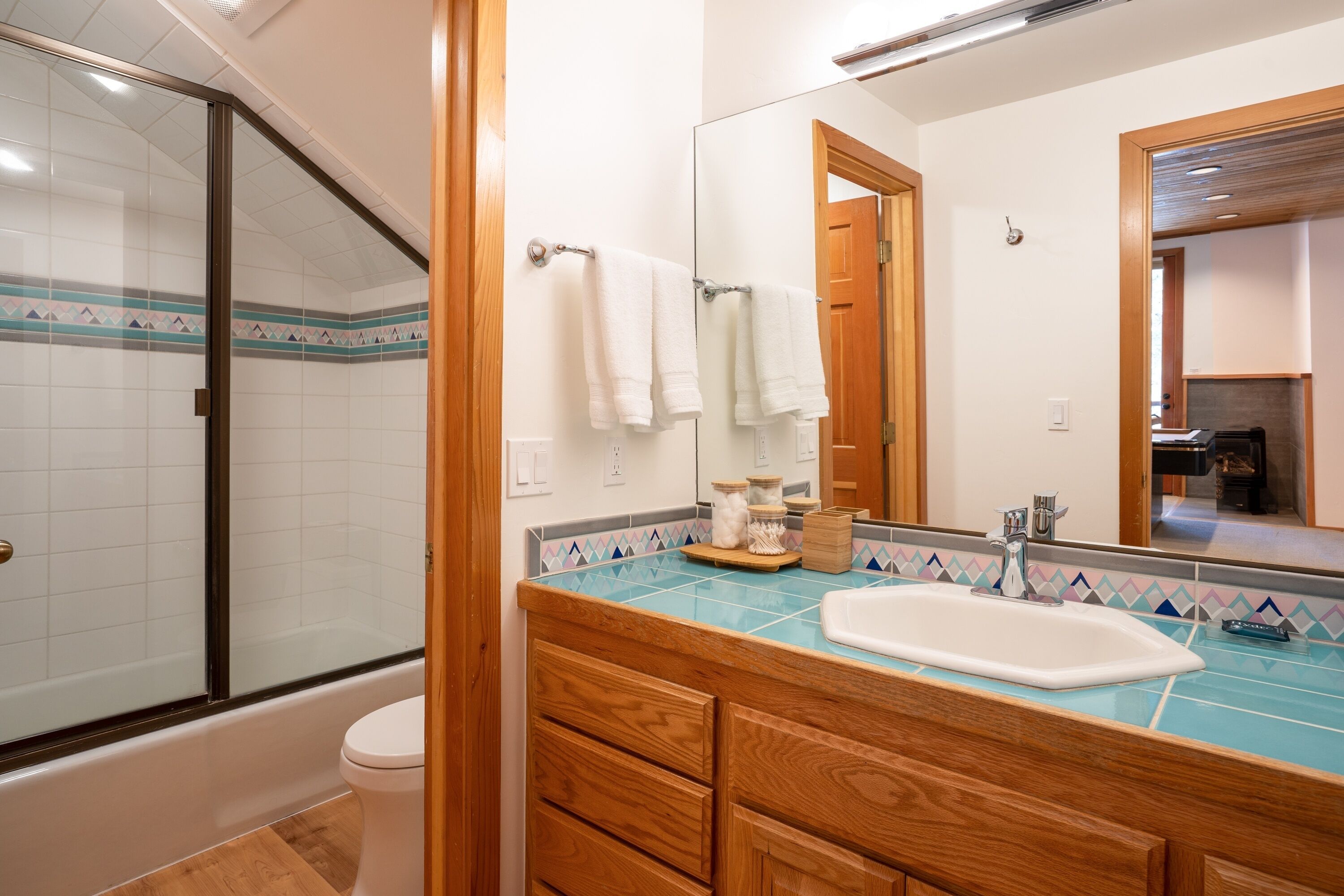 A bathroom with a glass shower enclosure, a white toilet, a wooden vanity with a sink, and a mirror above the vanity.