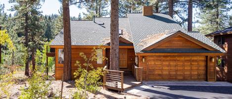 Une cabane en rondins avec un garage, entourée d’arbres et bordée d’une allée en gravier.