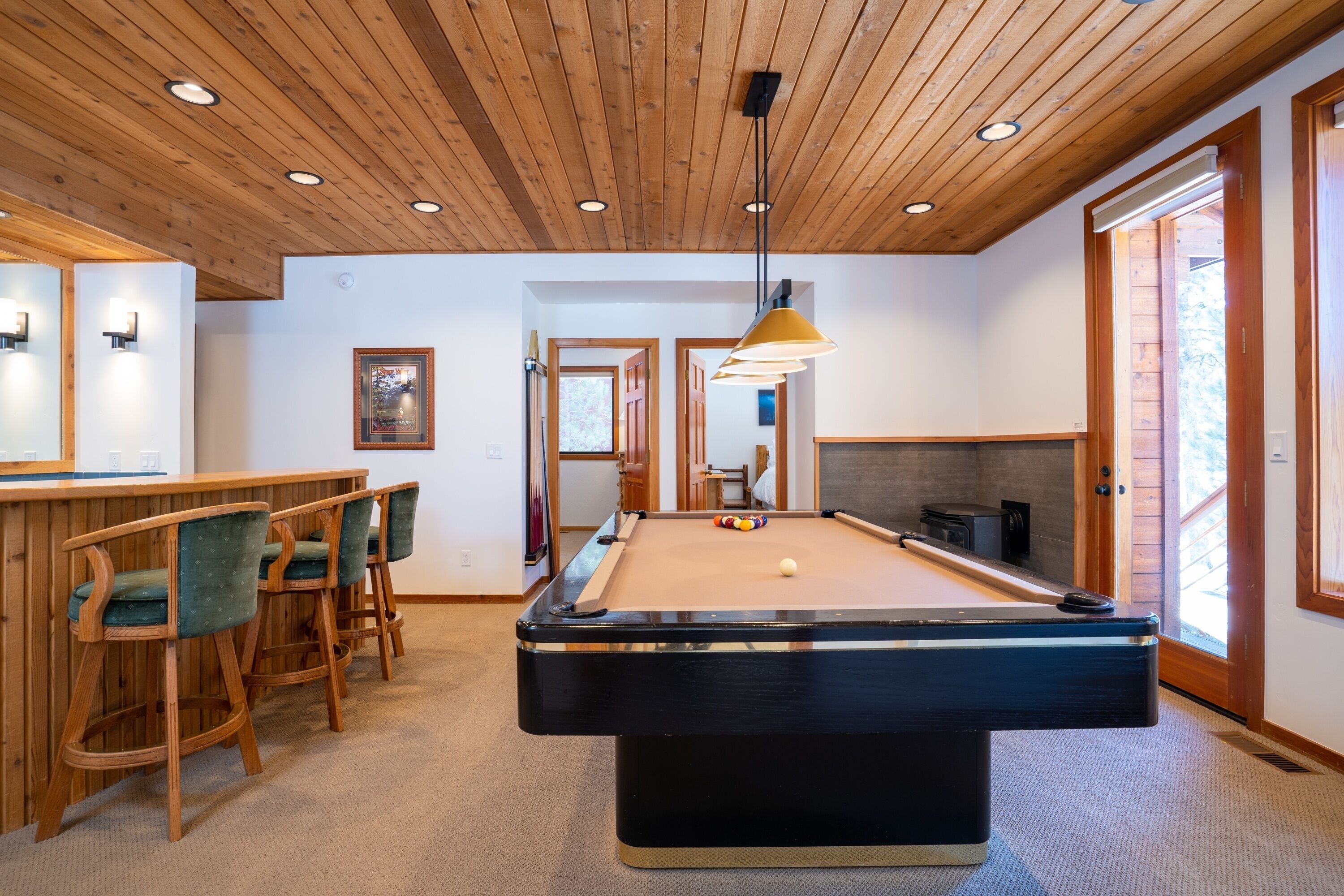 A pool table with chairs, a bar area, and a wooden ceiling.
