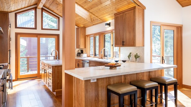 A spacious kitchen with wooden cabinetry, a large island with bar stools, and large windows providing natural light.