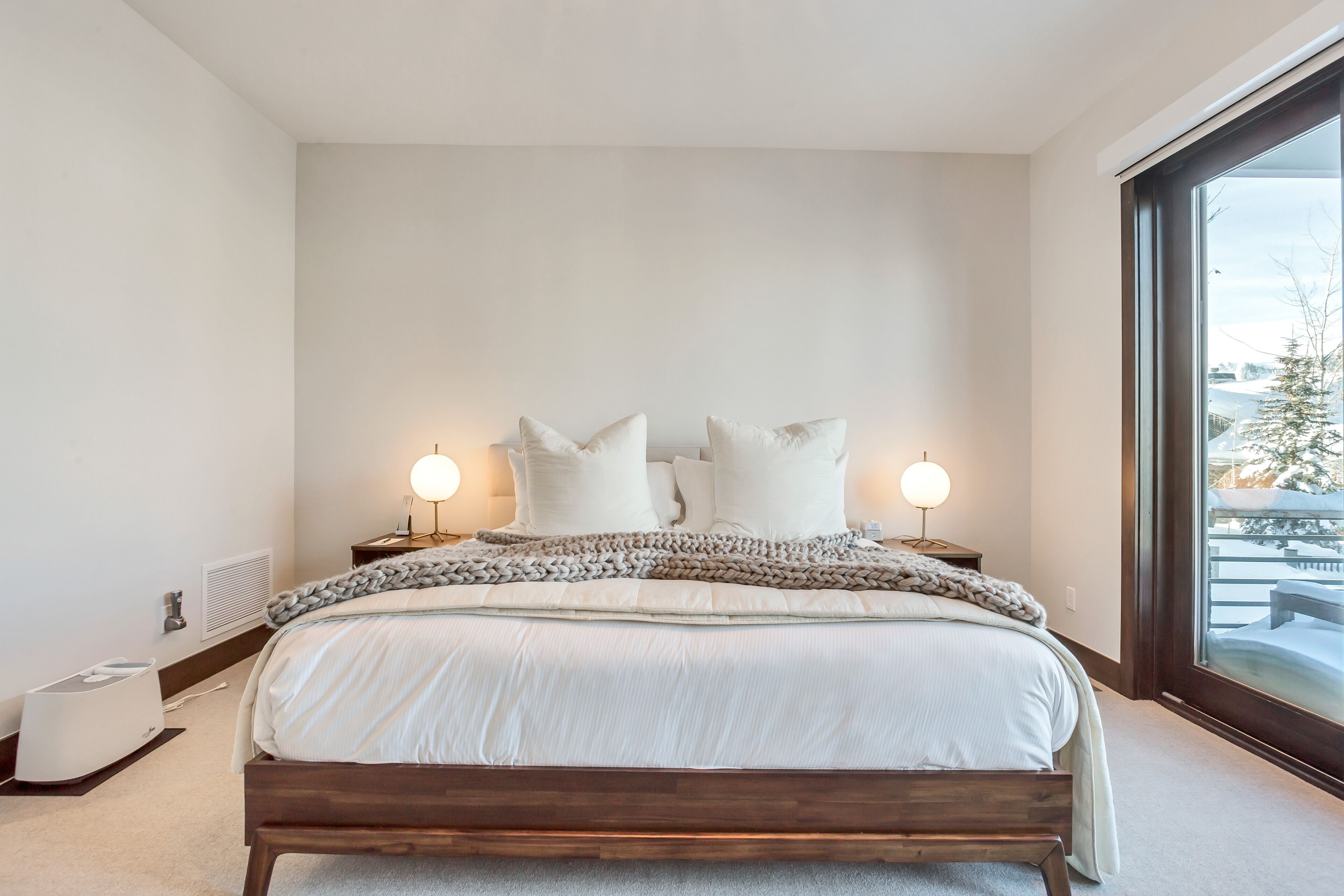 A modern bedroom with a large bed, two bedside lamps, and a view of a snowy outdoor area.