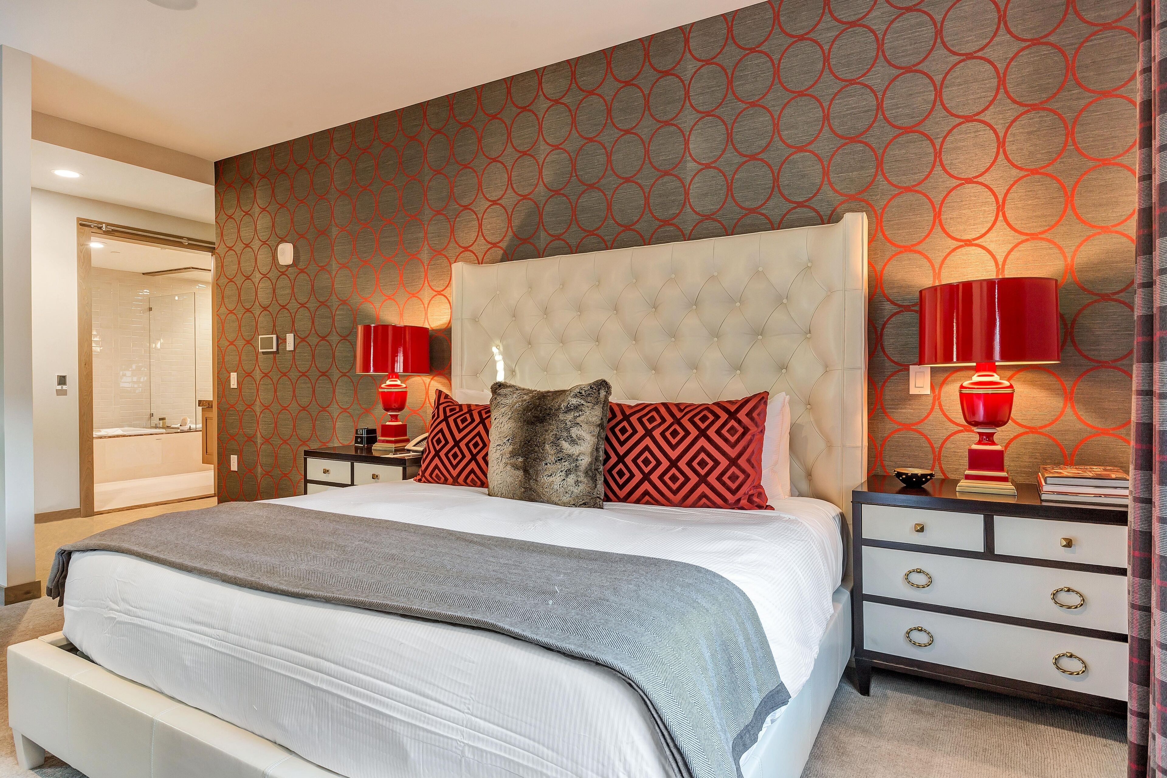 Une chambre à coucher moderne avec un grand lit, une tête de lit, deux tables de chevet avec des lampes et un mur décoré d’un motif.