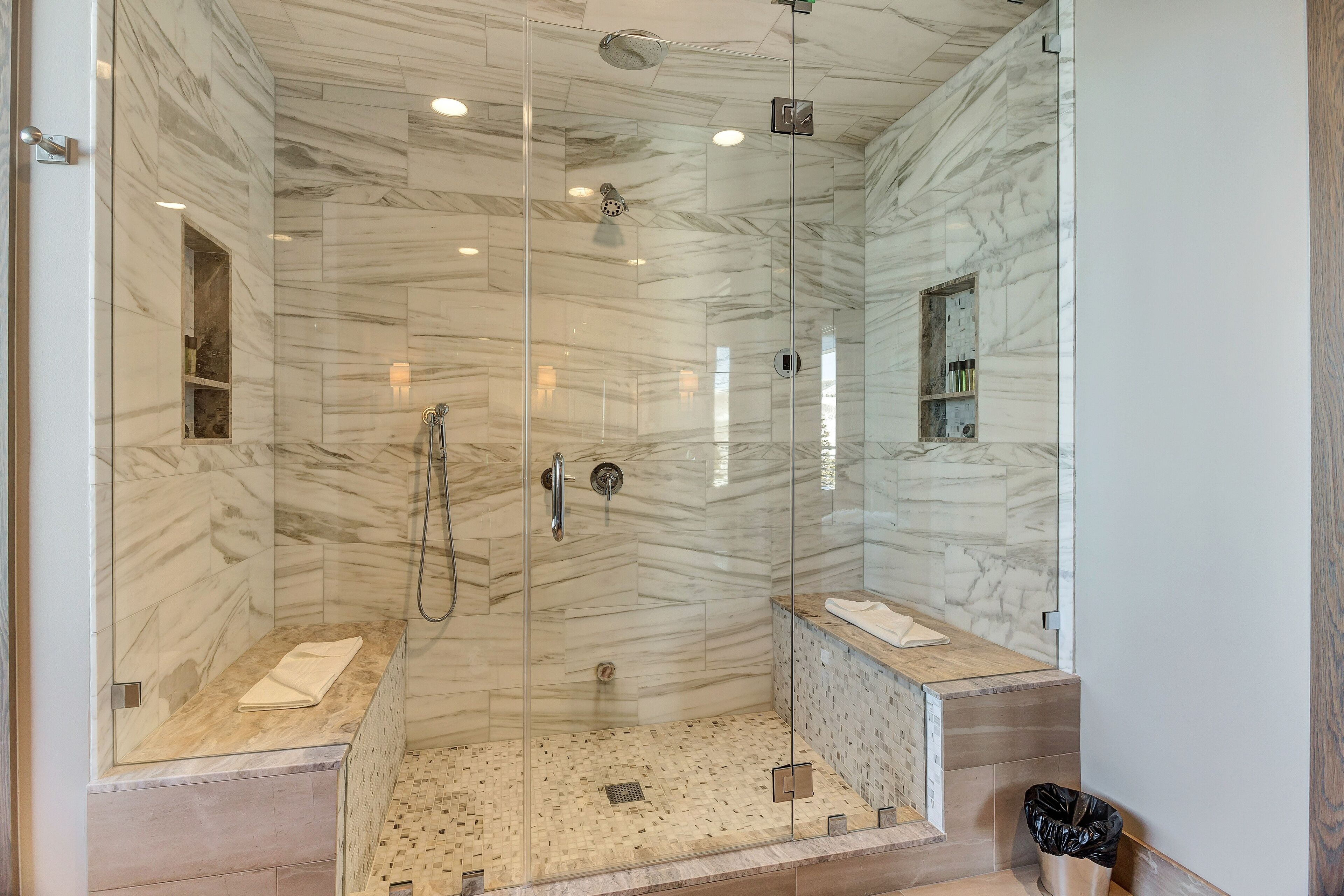 A modern bathroom with a glass-enclosed shower, marble walls, and a wooden vanity.