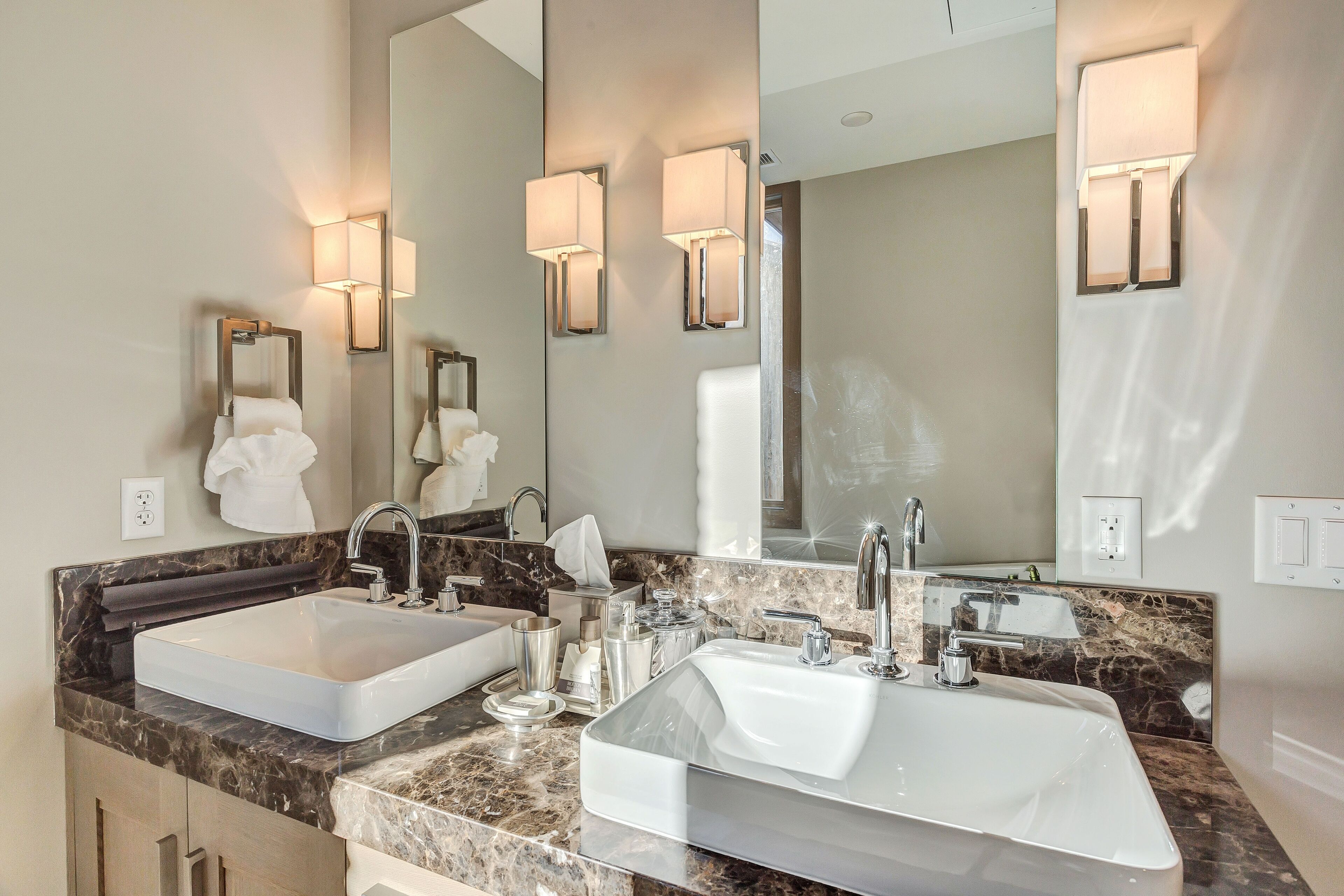 A modern bathroom with two sinks, marble countertops, and wall-mounted lighting.