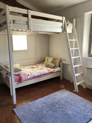Uma cama beliche com escada, uma janela pequena e um radiador.