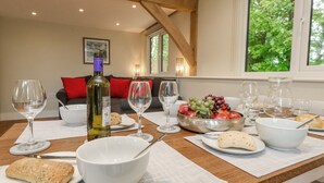 A dining table set with wine glasses, bowls, and plates of food, with a view of a living room in the background. - Roman Lodge (Weymouth)