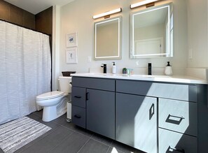 A modern bathroom with a toilet, bidet, vanity with a mirror, and a shower curtain. - Downtown Two Suite Penthouse 411 (Traverse City)