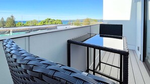 Un balcon avec un fauteuil en osier, une vue sur la mer et un bâtiment à la façade blanche.