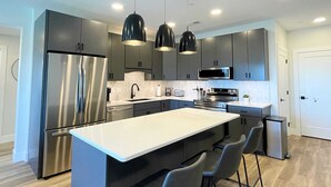 Une cuisine moderne dotée d’un îlot central, d’appareils électroménagers en acier inoxydable et de sièges de style bar.