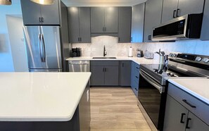 Una cocina moderna con armarios grises, electrodomésticos de acero inoxidable y encimera blanca.