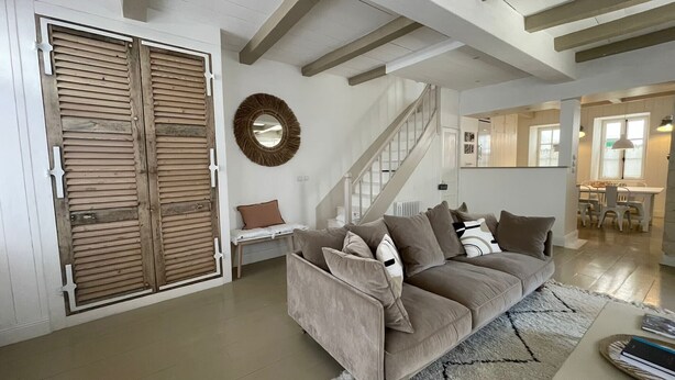 A living room with a sofa, a round mirror, a staircase, and a dining area.
