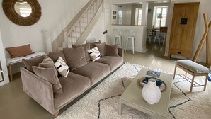 A spacious living room with a high ceiling, a staircase, a sofa, a coffee table, and a dining area in the background.
