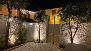 A stone-floored courtyard with a gated entrance, illuminated by string lights and a warm light source.