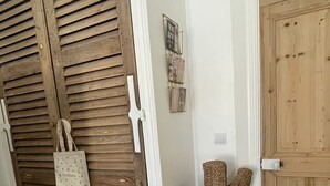 A room with a wooden door, a woven chair, and a wall-mounted picture frame.