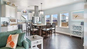 A spacious kitchen with white cabinets, a dining area with wooden chairs, and a view of the backyard through large windows.