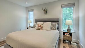 A bedroom with a large bed, a ceiling fan, two bedside tables with lamps, and a decorative wall piece.