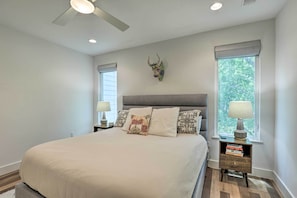 A bedroom with a large bed, a ceiling fan, two bedside tables with lamps, and a decorative wall piece.